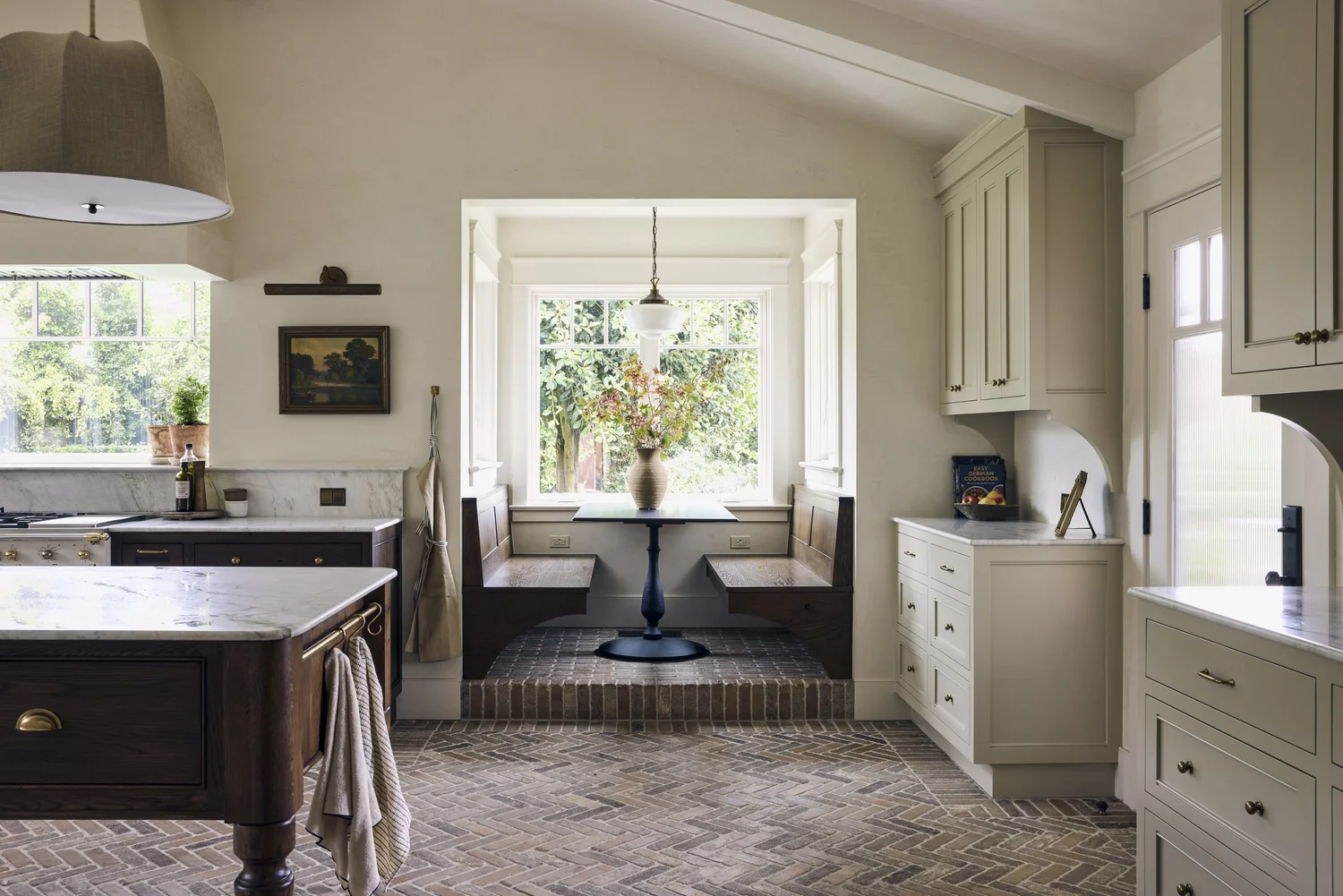 Farmhouse kitchen with a dark wood island, brick floor, and a window-lit breakfast nook