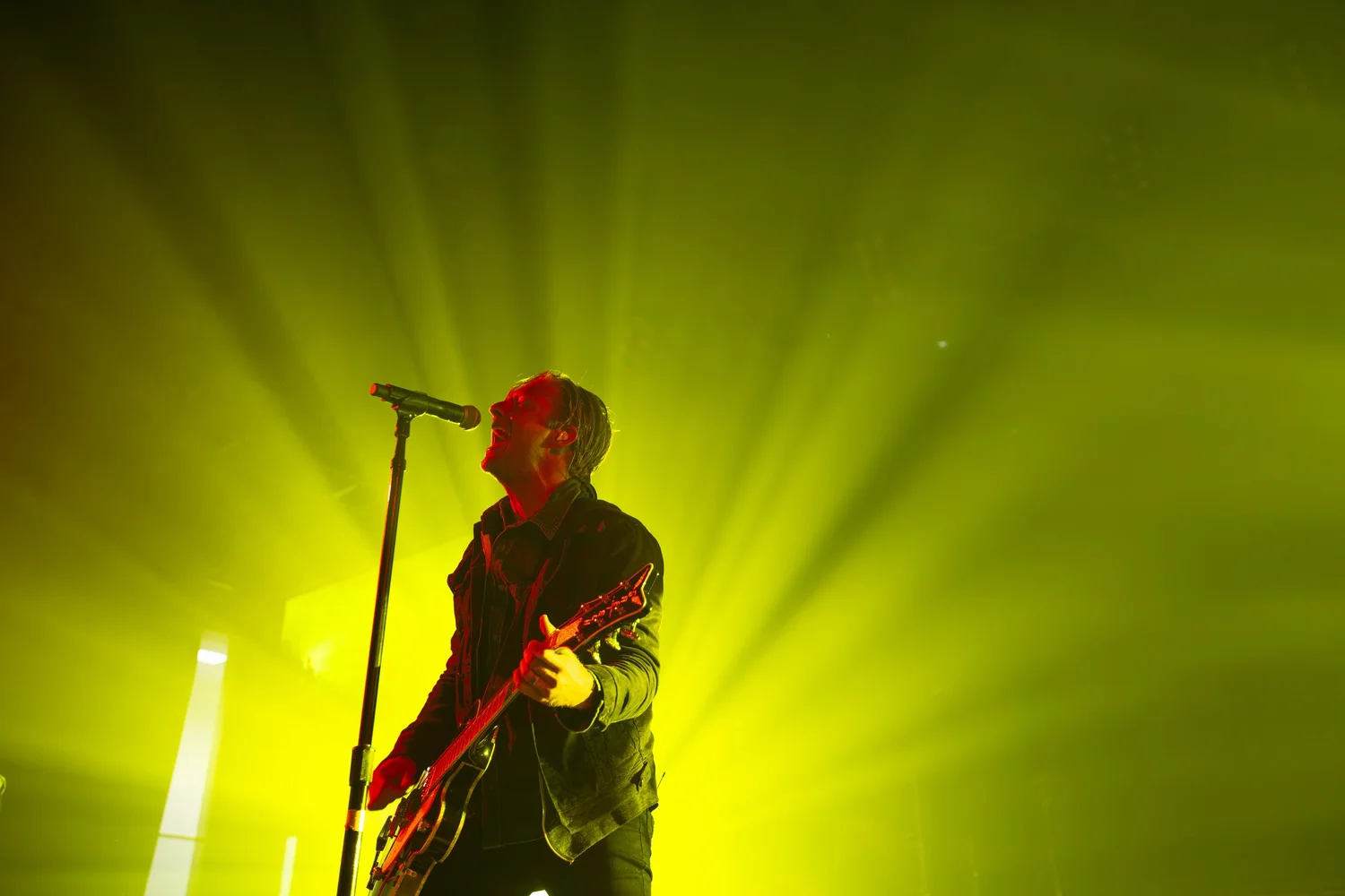 Switchfoot frontman singing and playing guitar on stage under bright yellow concert lights