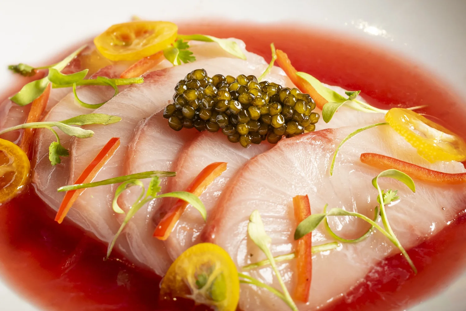 Vibrato hamachi crudo topped with caviar, citrus, and microgreens in a red broth