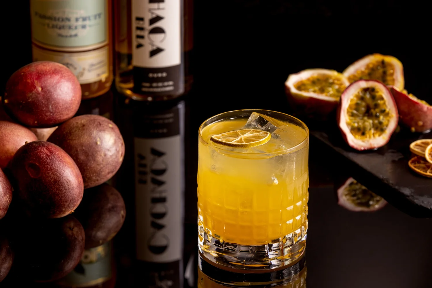 Vibrato passion fruit cocktail in a crystal glass beside halved passion fruit and liquor bottles